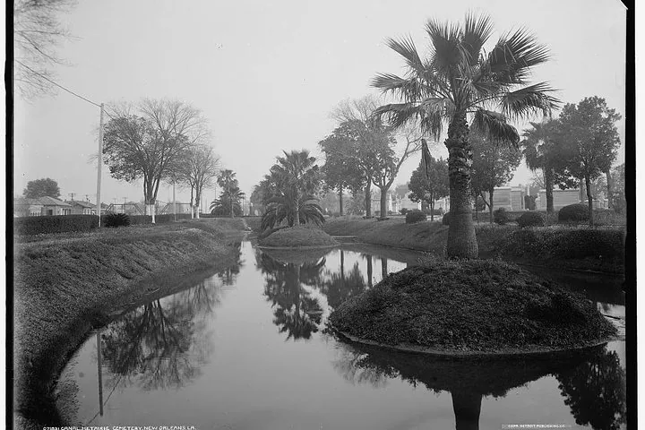 A vintage view of a tranquil canal surrounded by palm trees in Metairie Cemetery.