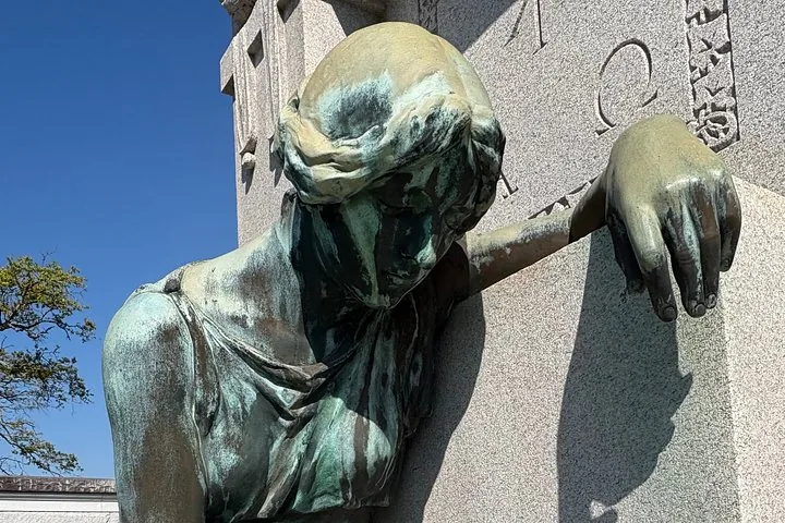 Close-up of a bronze statue leaning against a tomb.