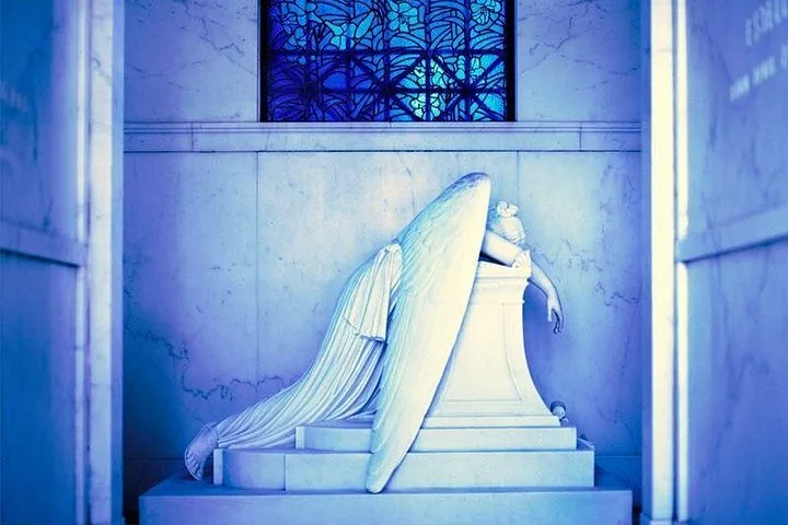 A weeping angel statue leaning on an altar inside a tomb.