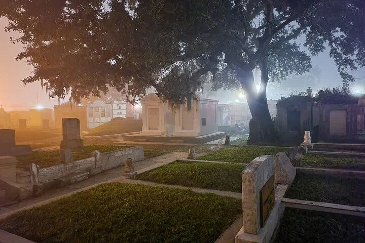 Above-ground tombs and large oak trees in a cemetery at night.