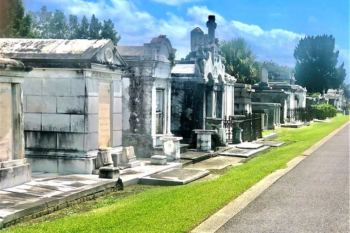 A row of impressive stone mausoleums alongside a grassy strip in Metairie Cemetery.