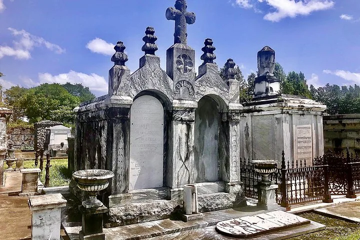 An ornate marble tomb at Metairie Cemetery under a blue sky.