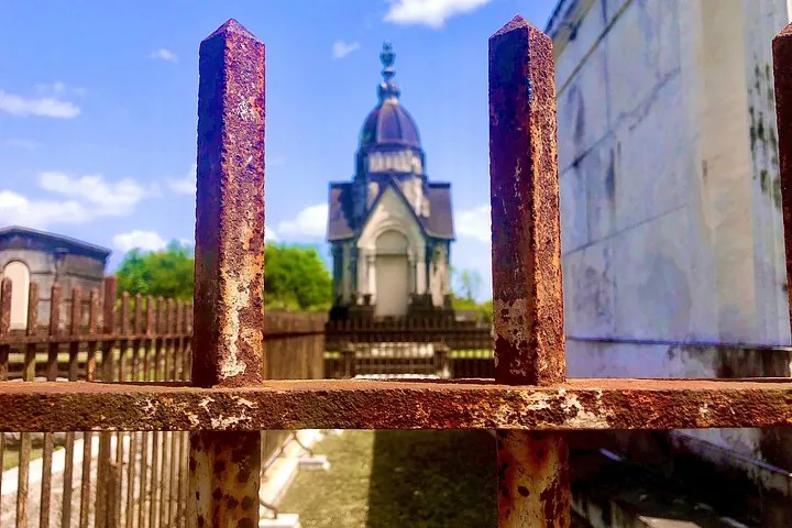 A blurry tomb building viewed through a rusted iron fence.