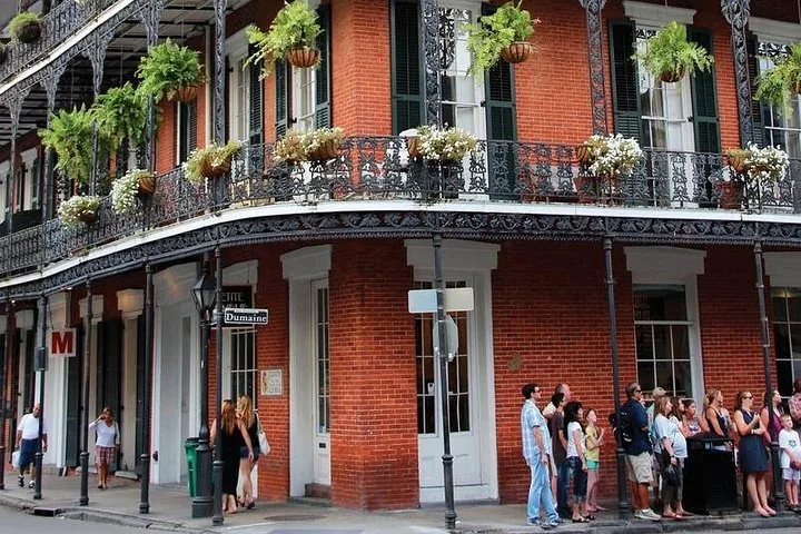People standing outside a red brick building with ornate wrought-iron balconies.